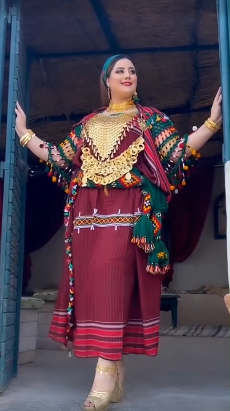 Burgundy Kurdish dress worn with a colourful tasselled shawl and a gold coin piece across the chest